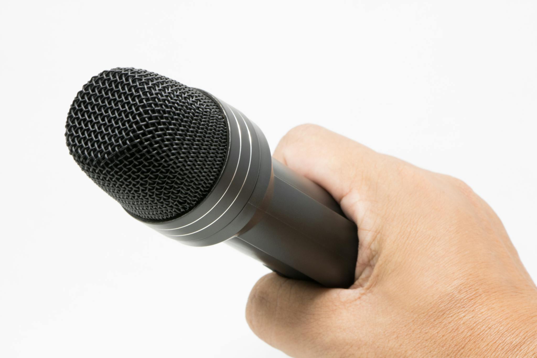 A close-up image of a hand holding a microphone against a plain background, showcasing audio equipment.