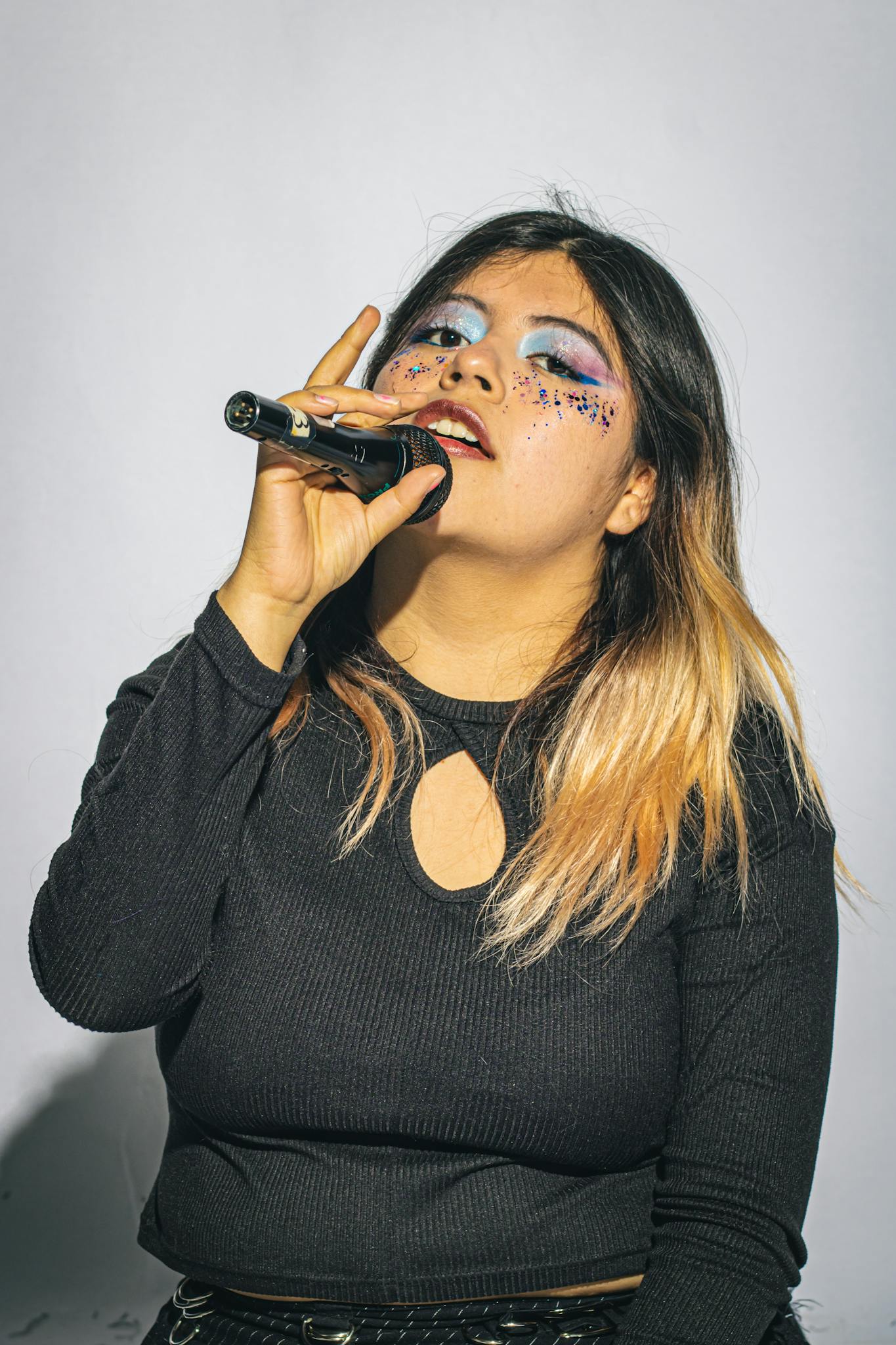 Young woman with bold artistic makeup singing passionately into a microphone.